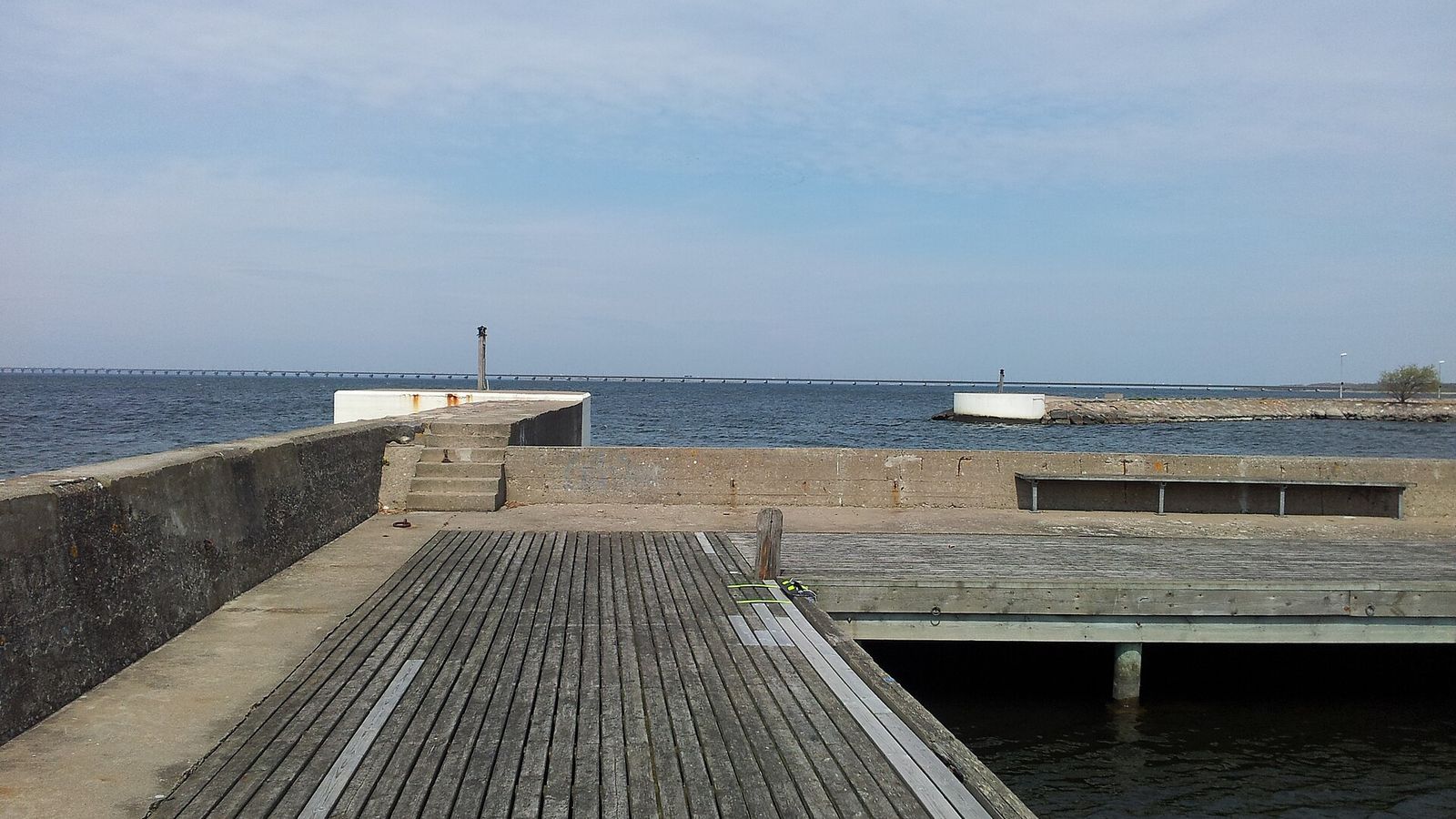 Träbrygga och vågbrytare i en svensk småbåtshamn med öppet vatten utanför