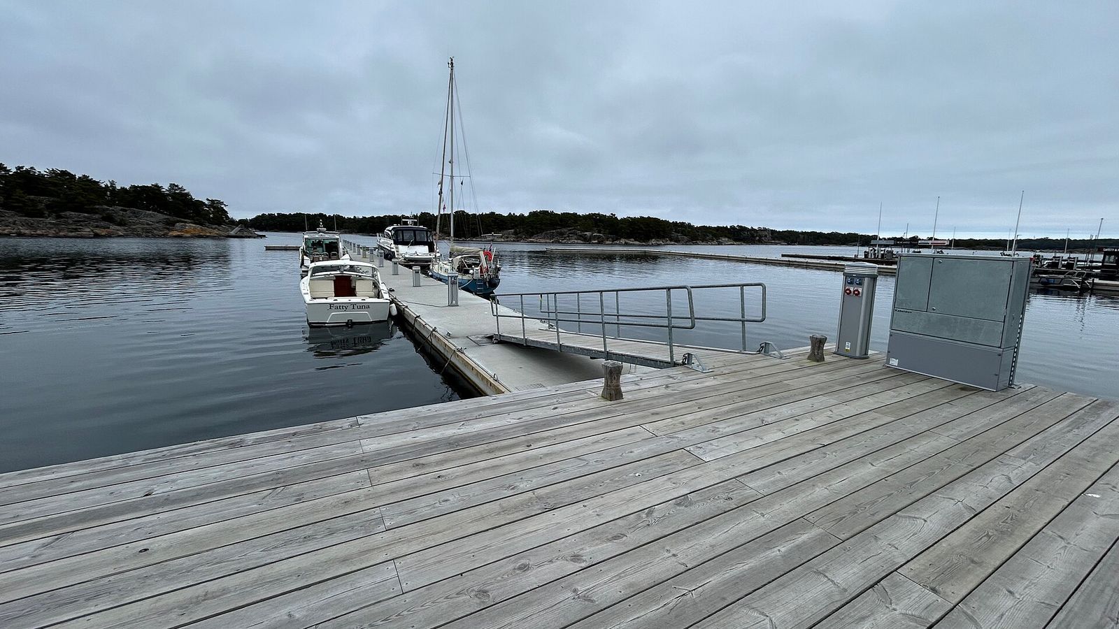 Träbrygga i Sandhamn med förtöjda båtar under en mulen sommarhimmel