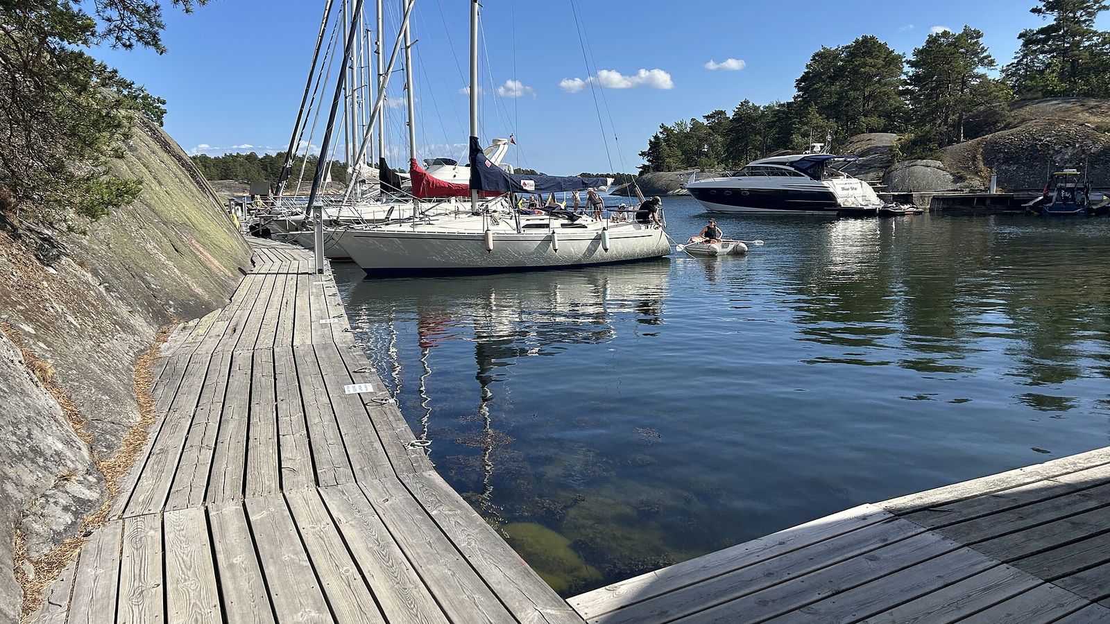 Träbrygga längs en klippa med segelbåtar förtöjda i en skyddad skärgårdshamn
