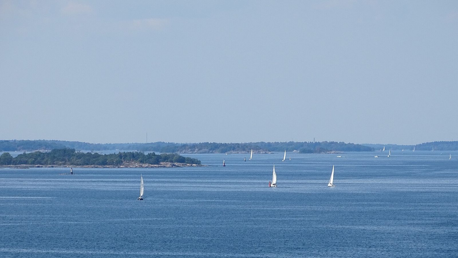 Segelbåtar på en öppen fjärd i Stockholms skärgård med låga öar vid horisonten