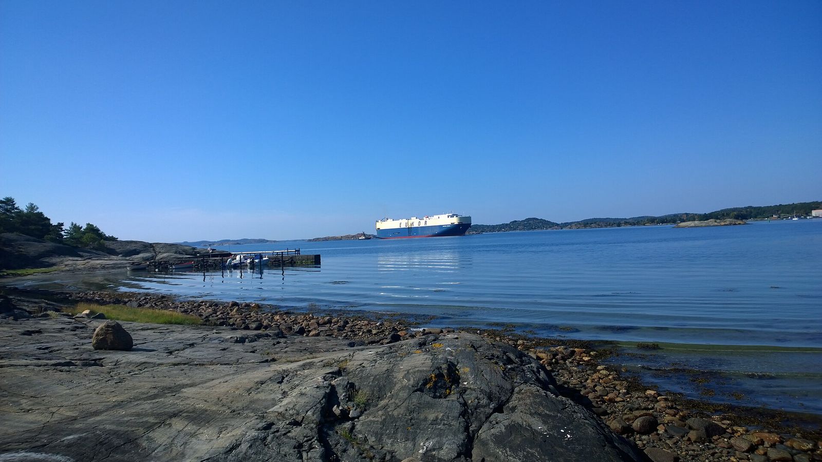 Klippstrand på Tjörns insida med ett bilfartyg på väg mot Wallhamn